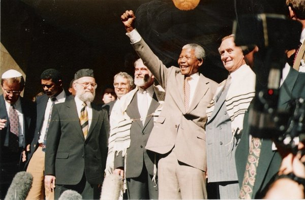 Nelson Mandela saluted the crowd at the Green and Sea Point Hebrew Congregation in Cape Town in 1994, joined by (from left) Rabbi Jack Steinhorn; Israel’s ambassador to South Africa, Alon Liel; Chief Rabbi Cyril Harris; and Mervyn Smith, chairman of the South African Jewish Board of Deputies; 